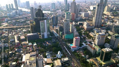 BTS Skytrain in Bangkok drives into Surasak station in the business district. Aerial drone shot from above. Busy street with many cars, traffic, and Skyscrapers on a sunny day. public transport. photo