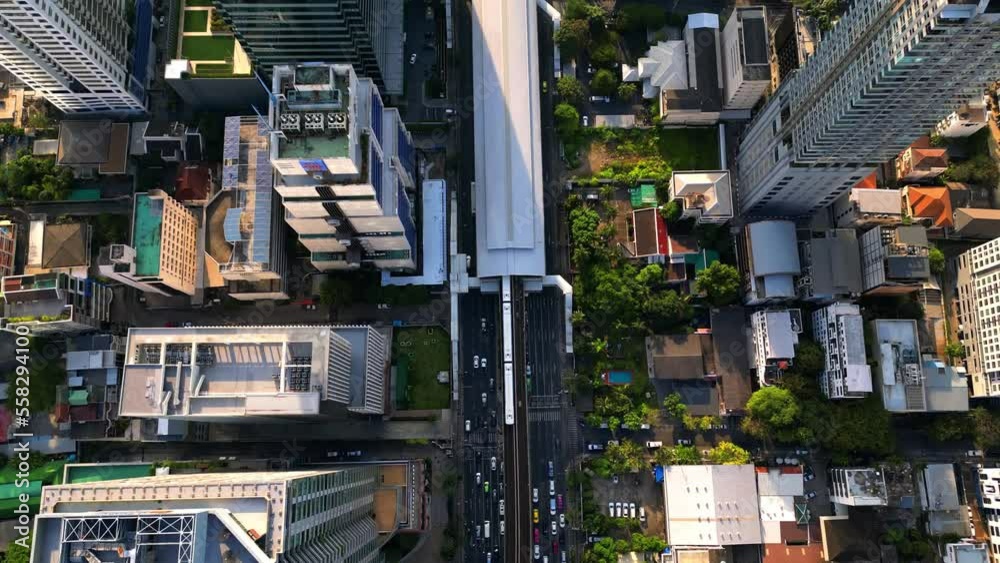 BTS Skytrain in Bangkok drives into Surasak station in the business district. Aerial drone shot from above. Busy street with many cars, traffic, and Skyscrapers on a sunny day. BTS Skytrain in Bangkok drives into Surasak station in the business district. Aerial drone shot from above. Busy street with many cars, traffic, and Skyscrapers on a sunny day.