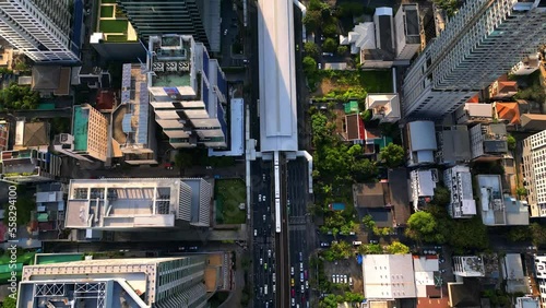 BTS Skytrain in Bangkok drives into Surasak station in the business district. Aerial drone shot from above. Busy street with many cars, traffic, and Skyscrapers on a sunny day. photo