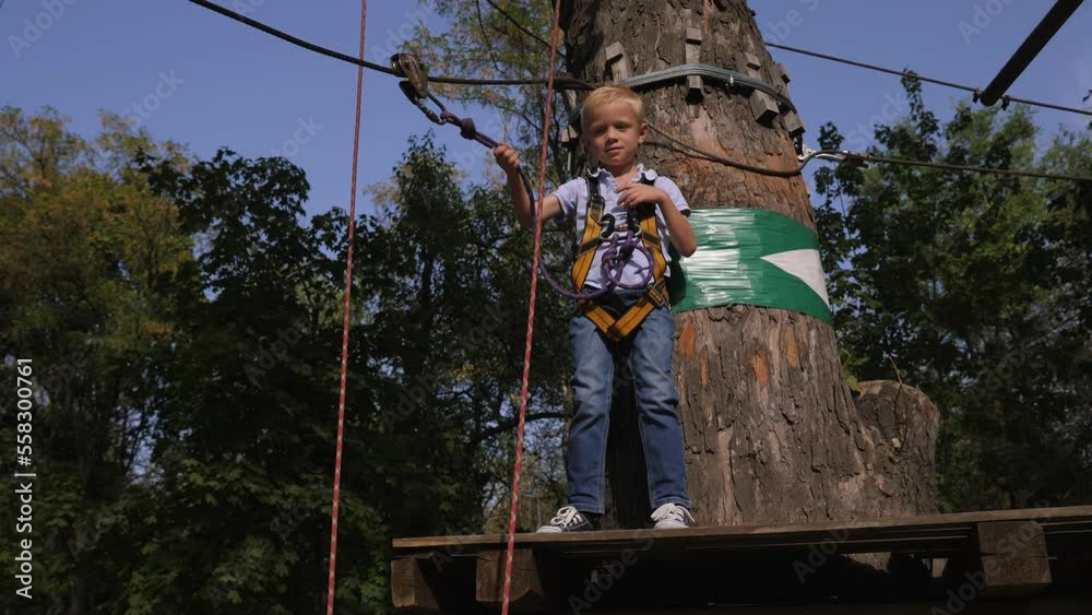 A small six-year-old boy Braves obstacles in a rope Park between trees in the summer. A small six-year-old boy Braves obstacles in a rope Park between trees in the summer.