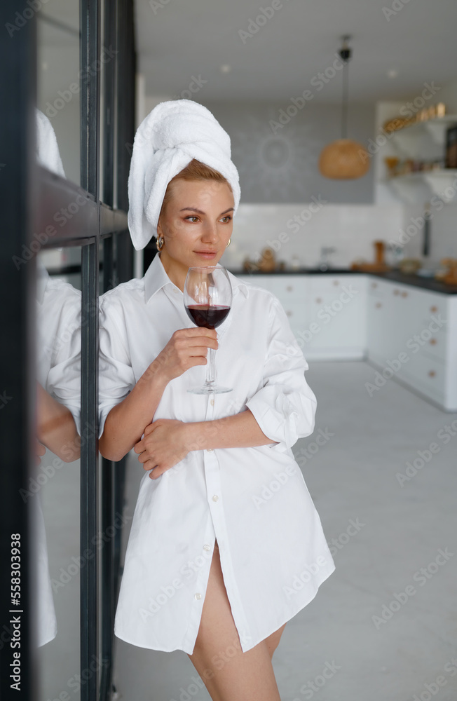 Beautiful woman in towel drinking wine from glass on home kitchen