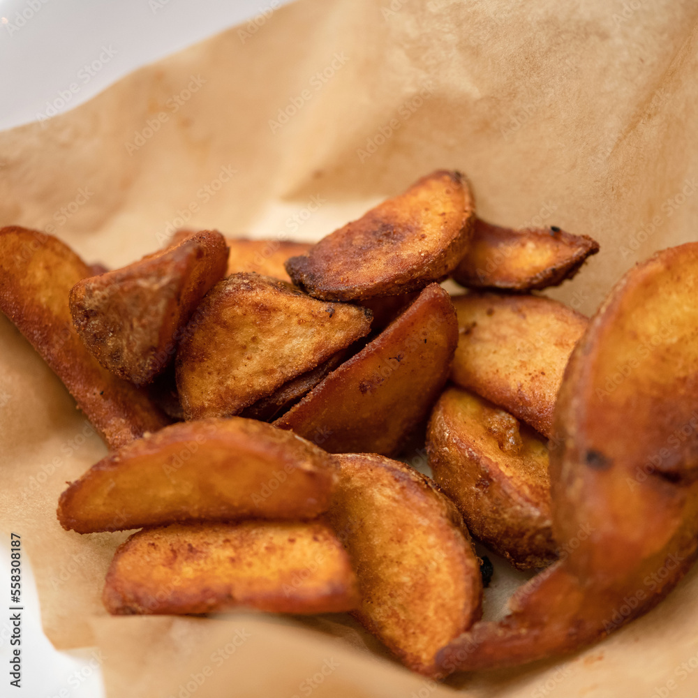 Fried potato wedges on baking paper. French fries. Oven baked. Vegetable garnish. Vegetarian dish. Rustic potatoes. Copy space. Close-up. Soft focus. Fried potato wedges on baking paper. French fries. Oven baked. Vegetable garnish. Vegetarian dish. Rustic potatoes. Copy space. Close-up. Soft focus.