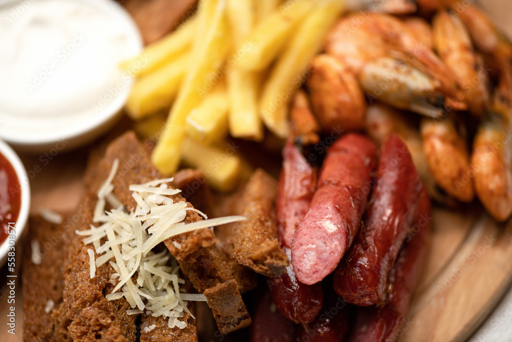 French fries, sausages, shrimp, bread, cheese, sauce on wooden board. Fries menu. Fast food. Plate of snacks. Close-up. Soft focus. French fries, sausages, shrimp, bread, cheese, sauce on wooden board. Fries menu. Fast food. Plate of snacks. Close-up. Soft focus.