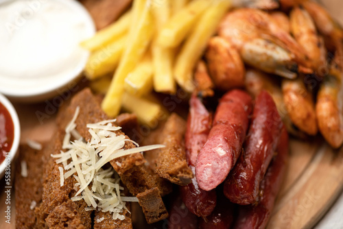 French fries, sausages, shrimp, bread, cheese, sauce on wooden board. Fries menu. Fast food. Plate of snacks. Close-up. Soft focus.