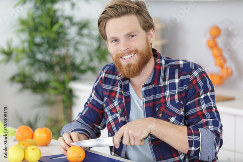 handsome man cutting orange by knife on kitchen