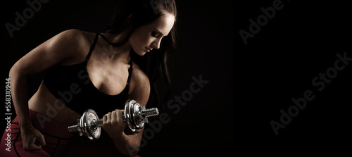 Beautiful young woman works out with dumbbells in fitness gym