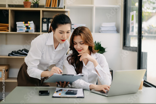 Two Asian businesswoman discuss investment project working and planning strategy with tablet laptop computer in modern office..