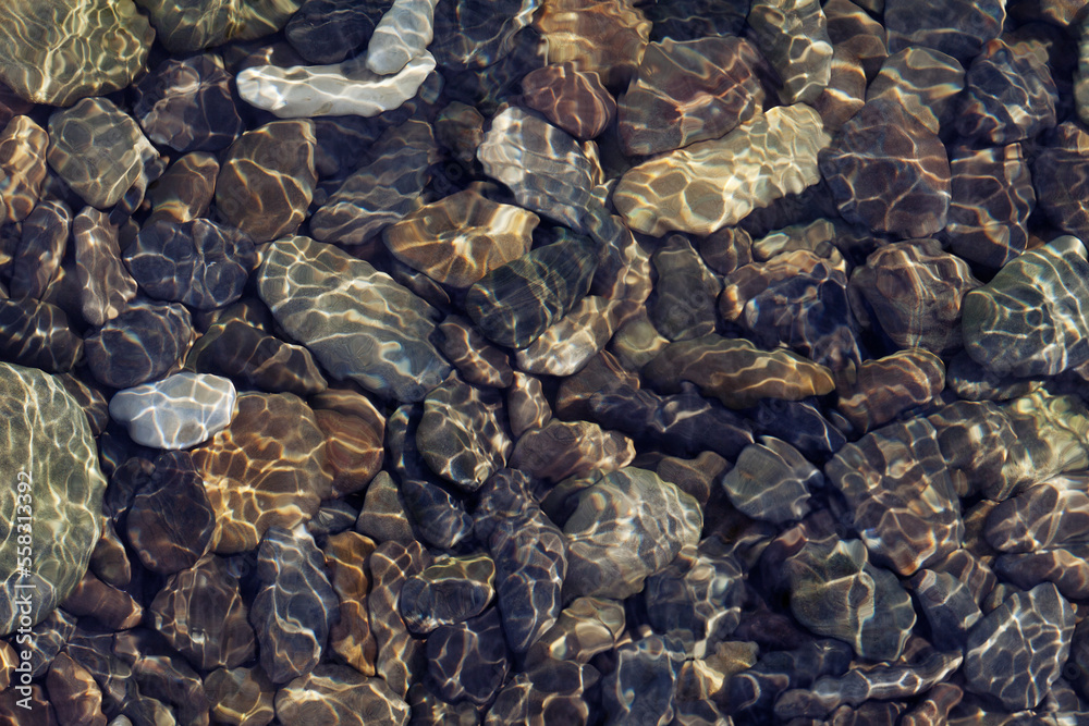 Ripple patterns reflect light on shallow flowing clear water over pebbles