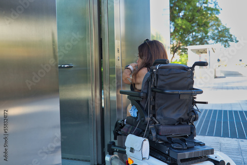 Disabled woman with reduced mobility and small stature in an electric wheelchair trying to enter an elevator. Concept handicap, disability, incapacity, special needs, architectural barriers.