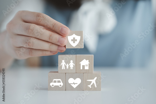 Insurance concept. Protection against a possible eventuality. Hand holding security symbol and house, car, family, travel and health care on wooden block. Life assurance concept.