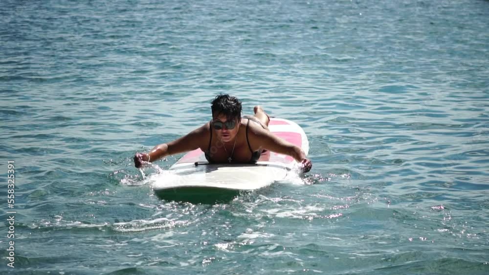 Happy body positive woman smiling and paddling on her surfboard in ocean or sea to beach after surfing on sunny day. Modern individual female hipster outdoor summer sport activity. Slow Motion Happy body positive woman smiling and paddling on her surfboard in ocean or sea to beach after surfing on sunny day. Modern individual female hipster outdoor summer sport activity. Slow Motion