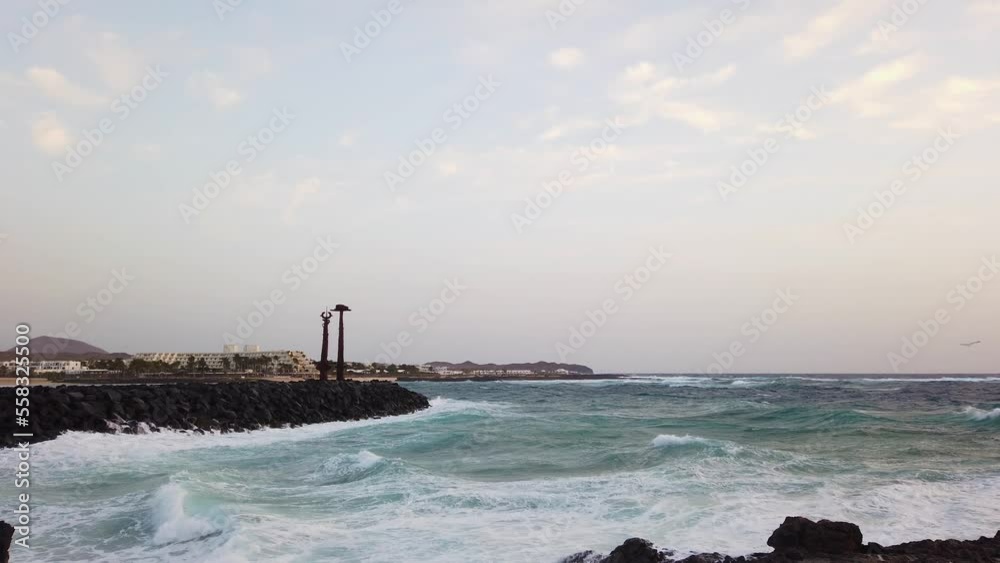Storm on Lanzarote island, view of Costa Teguise coastline with powerful blue waves splashing on volcanic lava rocks like tsunami, and birds flying against wind. Costa Teguise, Canary Islands, Spain. Storm on Lanzarote island, view of Costa Teguise coastline with powerful blue waves splashing on volcanic lava rocks like tsunami, and birds flying against wind. Costa Teguise, Canary Islands, Spain.