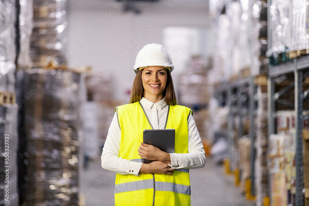 Portrait of a proud businesswoman standing in warehouse in protective work wear with tablet in her hands and smiling at the camera. Portrait of a proud businesswoman standing in warehouse in protective work wear with tablet in her hands and smiling at the camera.