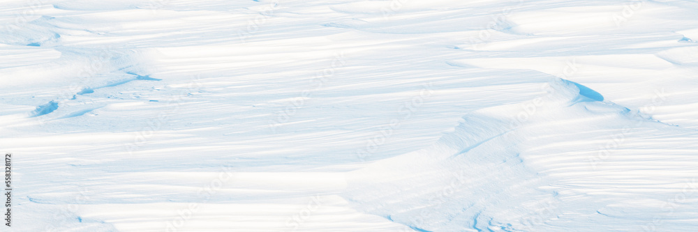 Wide panoramic winter background with snowy ground. Natural snow texture. Wind sculpted patterns on snow surface. Arctic, Polar region.