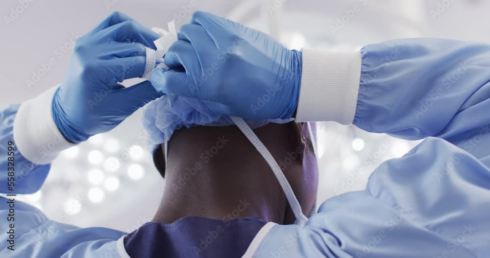 Back view of african american male surgeon in gloves tying face mask in operating theatre Back view of african american male surgeon in gloves tying face mask in operating theatre