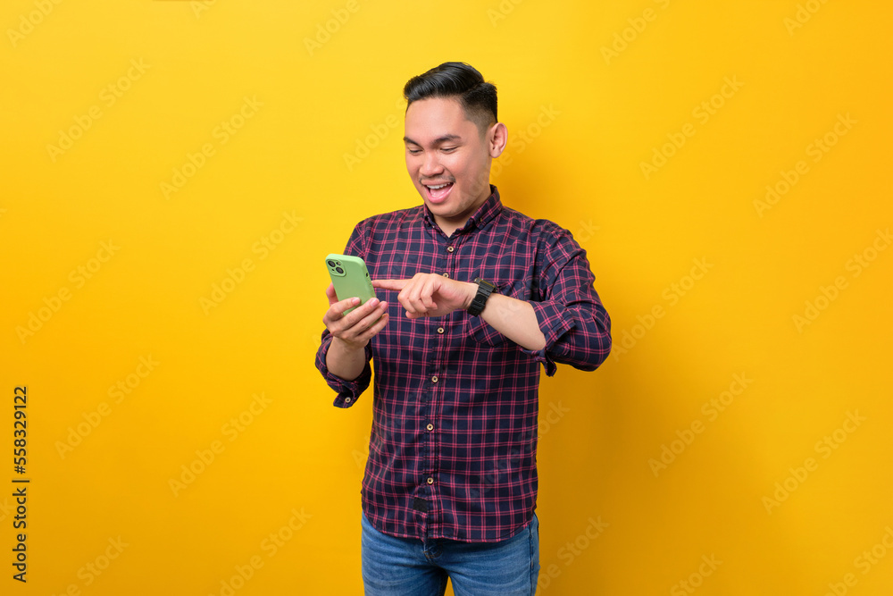 Smiling young Asian man using smartphone for browsing internet and scrolling social media news isolated over yellow background