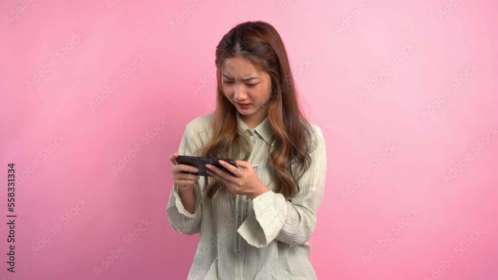 Young women smile and playing video game on smartphone with empty space on isolated pink background Young women smile and playing video game on smartphone with empty space on isolated pink background