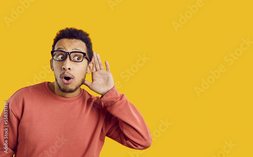 Leinwand Poster Young African American man isolated on yellow background hold hand at ear listen to news