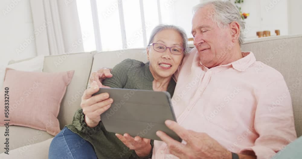 Happy diverse senior couple using tablet and sitting on couch Happy diverse senior couple using tablet and sitting on couch