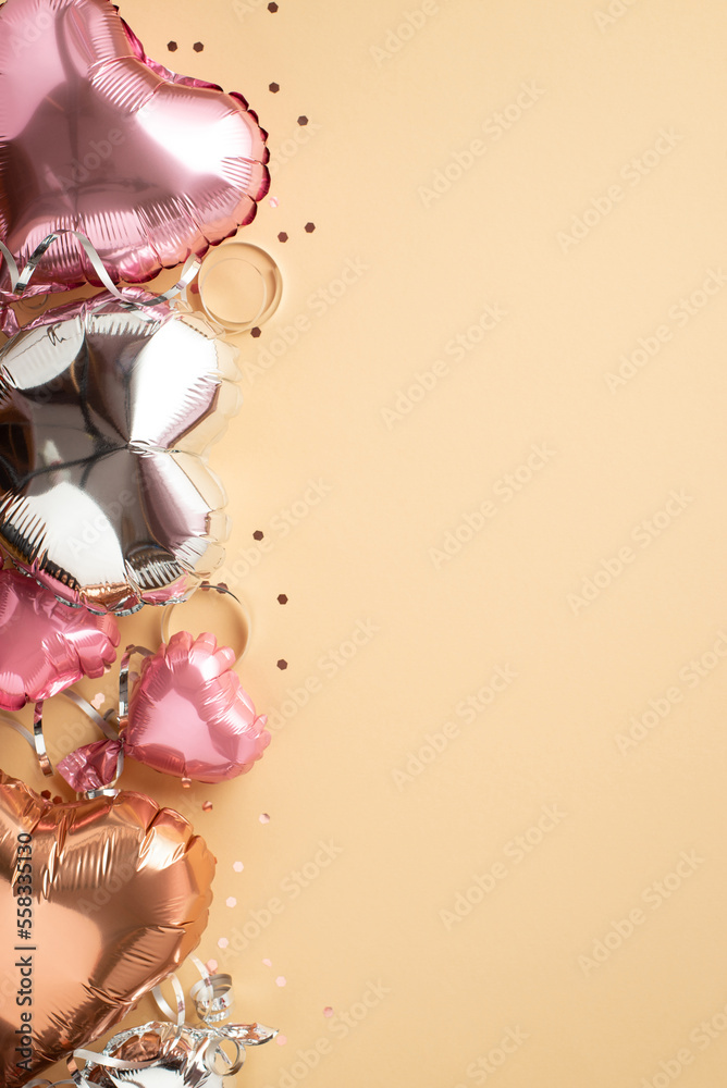 Fototapeta premium Valentine's Day decor concept. Top view vertical photo of stylish heart shaped balloons silver serpentine and shiny confetti on isolated pastel beige background with copyspace
