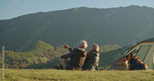 Mature caucasian couple travelling together after retirement, taking a rest on top of mountain, enjoying the view and talking - pension, recreational pursuit, tourism concept photo