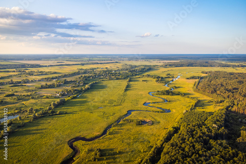 Valley of the river with small village on the background, aerial shot. Drone photo of small river near forest and village