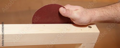 Wooden plank furniture handy sanding with Sandpaper circle in white carpenter hand closeup. photo