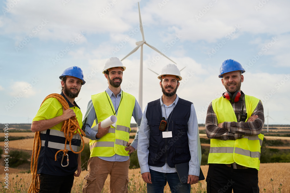 Portrait of a Group of smiling engineers looking at camera in an agricultural field with wind turbines. Outdoor power station. Renewable and clean energy concept, sustainable future. Portrait of a Group of smiling engineers looking at camera in an agricultural field with wind turbines. Outdoor power station. Renewable and clean energy concept, sustainable future.