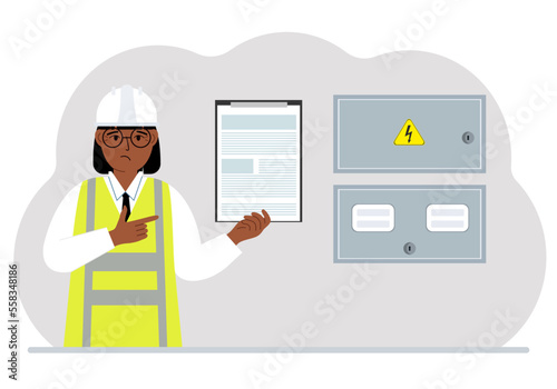 A female electrical engineer holds a clipboard with a contract and stands next to an electrical cabinet. The concept of a contract for service, connection of electricity or hiring a specialist.