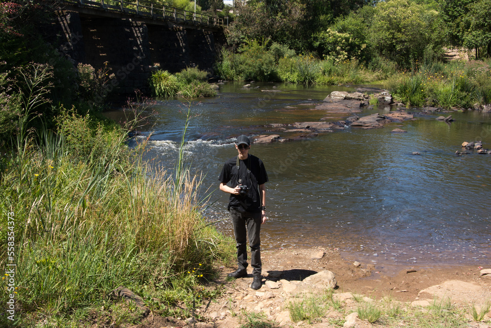 Young man on the riverbank with a camera in hand Young man on the riverbank with a camera in hand