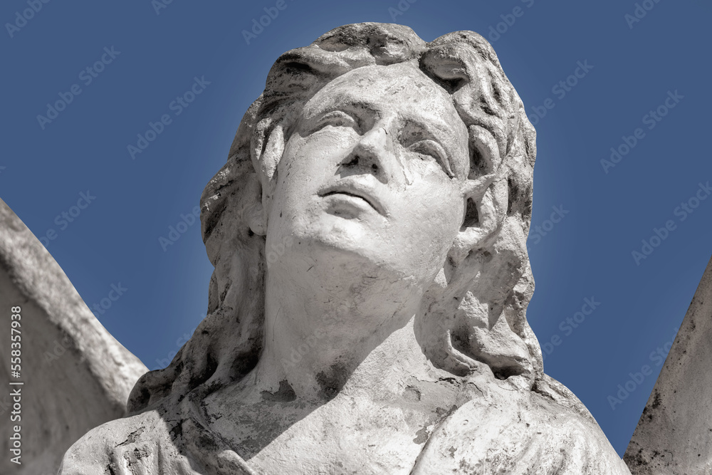 Fragment of ancient stone statue of angel against blue sky background.