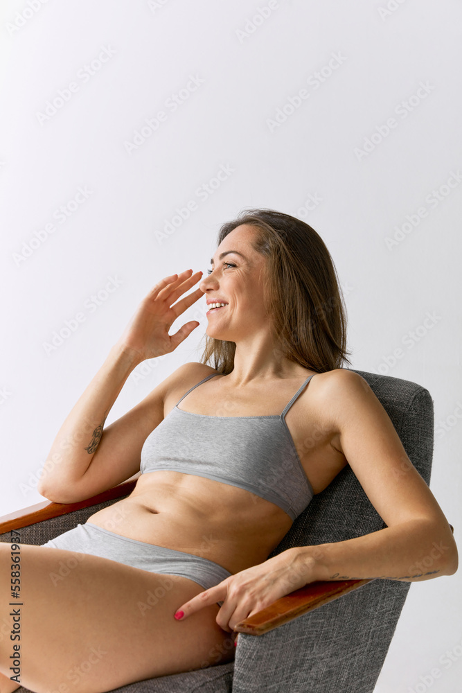 Portrait of beautiful woman sitting on chair and posing in underwear over grey studio background. Smiling Portrait of beautiful woman sitting on chair and posing in underwear over grey studio background. Smiling