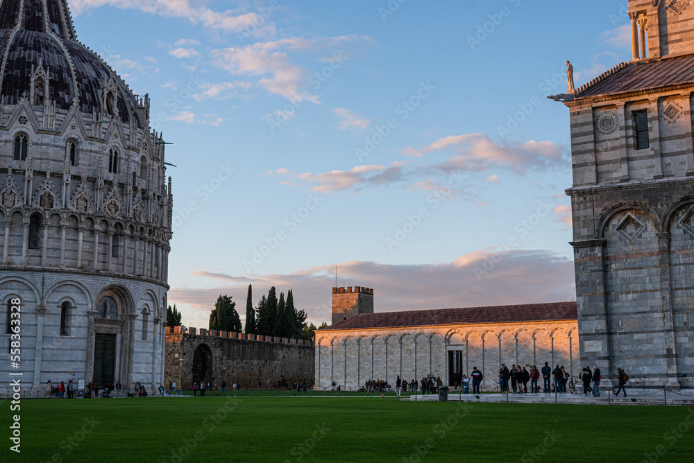 Low angle view of the baptistery, cathedral, museum, wall and large group of people against cloudy sky, sunset.
