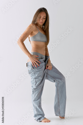 Full-length portrait of slim woman posing in top and jeans over grey studio background. Casual look