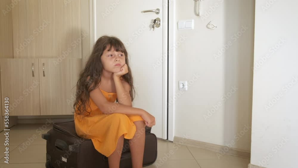 Refugee child with packed valise. A view of sad little girl sitting on her valise in the room. A concept of refugee problems during childhood. Refugee child with packed valise. A view of sad little girl sitting on her valise in the room. A concept of refugee problems during childhood.