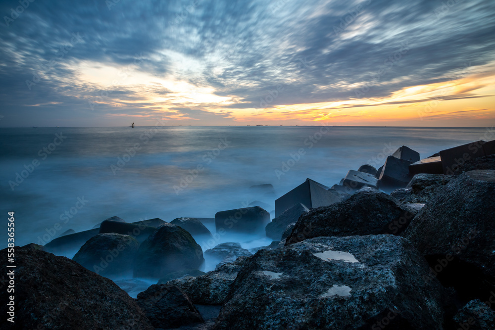 blue hour at the sea with cloudy sky and breakwater in the foreground long exposure