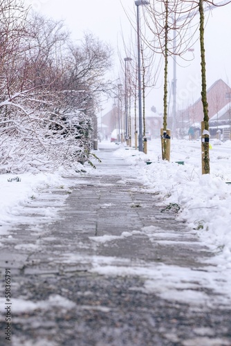 A portrait of a cleared sidewalk from snow made of stone tiles. The walk way is still covered with some frost and ice. If not cleared, the pavement is dangerous and slippery for pedestrians.