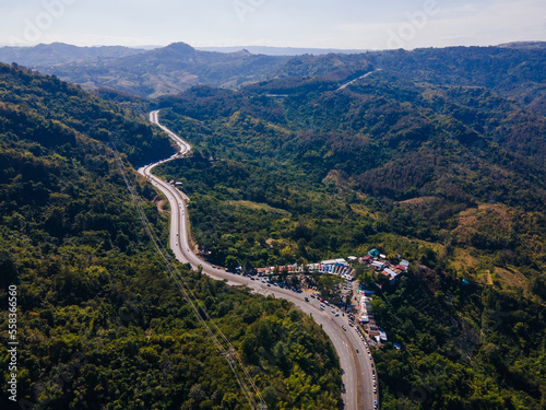 the aerial view of the countryside curve road near the green forest on the hill