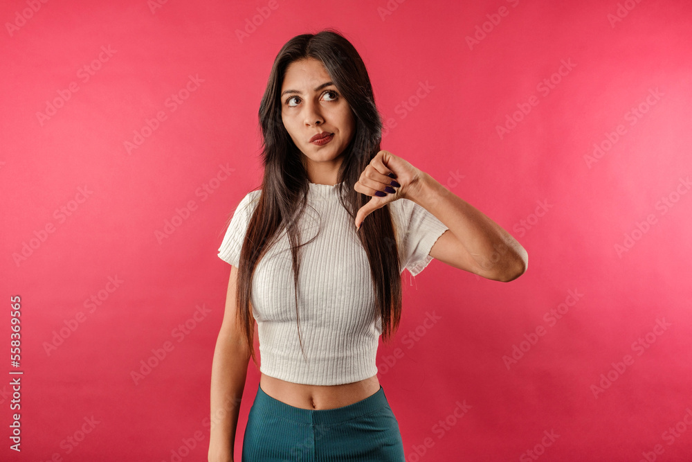 Young caucasian woman wearing casual top isolated over red background looking unhappy and angry showing rejection and negative with thumbs down gesture. Bad expression. Don't do it!