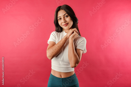 Brown-haired woman wearing white ribbed crop isolated over red background holding your hands looks hopefully at the camera  at you  and smiles.