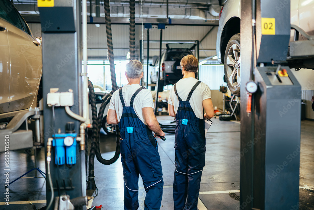Rearr view of two professional technicians of machine repair service in blue workwear. Car service, repair, maintenance and people concept. Rearr view of two professional technicians of machine repair service in blue workwear. Car service, repair, maintenance and people concept.