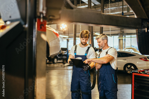 Mechanic man shows report on a tablet to the caucasian coworker at garage, A man mechanic and his son discussing repairs done vehicle. Changing automobile business.