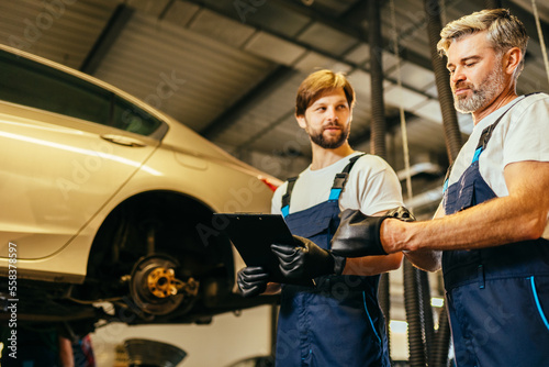 Two car mechanic diagnosing vehicle at the auto service. Car service, repair, maintenance and people concept. © Iryna