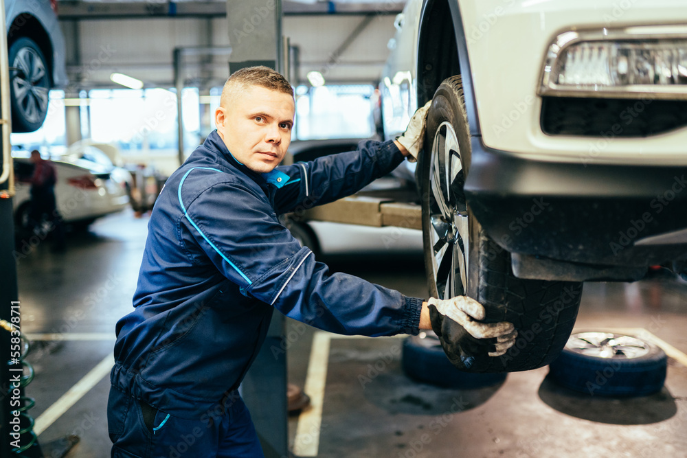 Male mechanic installing wheel on car in workshop. Auto car repair service center. Mechanic examining car suspension