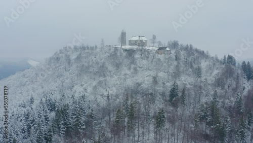 Aerial shot of a church on top of a mountain with a snowy forest in winter, in Slovenia