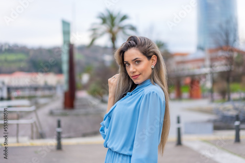 Portrait of blonde woman in blue dress walking along the river in the city, lifestyle concept