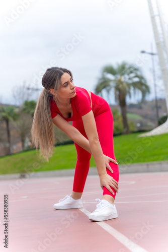 Fit woman in red outfit doing stretching in a city park, fitness and healthy active concept
