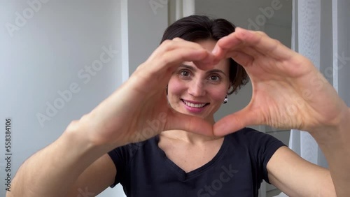 Close up happy smiling White Race woman make with fingers heart shape look at camera through symbol of love. Healthy heart health life insurance, love and charity, voluntary social work, organ donatio photo