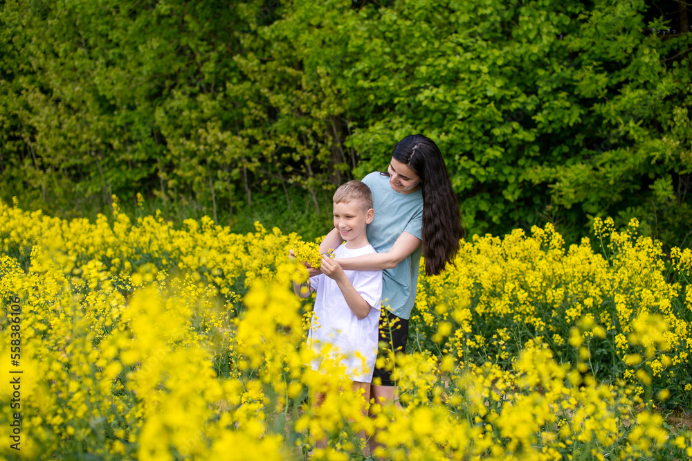 Fototapeta premium A young mother hugs her son in a field with yellow flowers