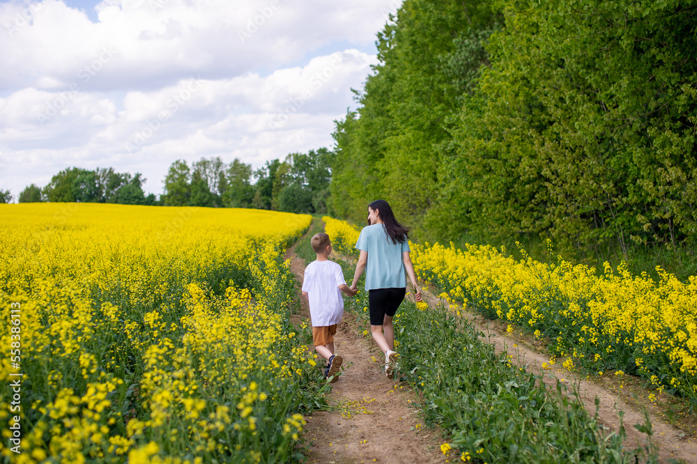Mom and son are running through the field with rapeseed. Yellow field
